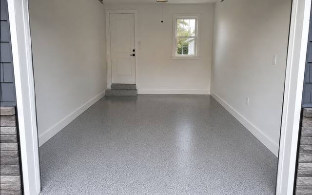 Grey flake garage floor coating in a single car garage with the door open to the driveway